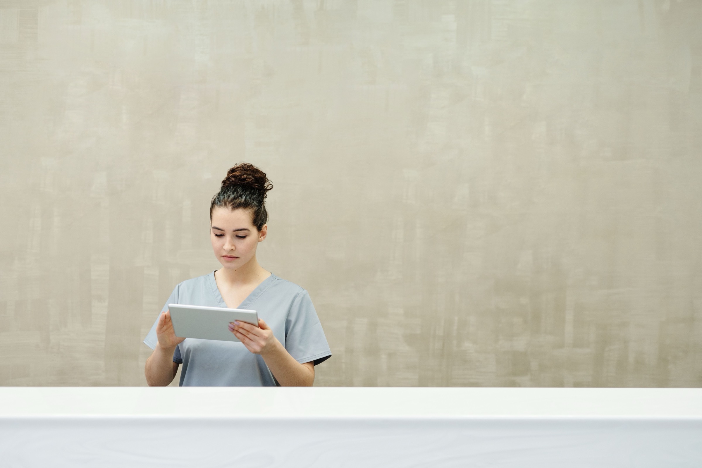 Eine Ordinationsassistentin steht an der Rezeption und liest auf einem Tablet